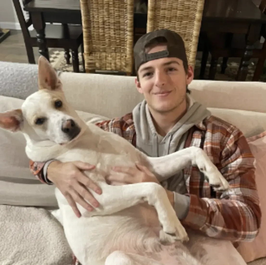 Man in cap holding small dog close to his face